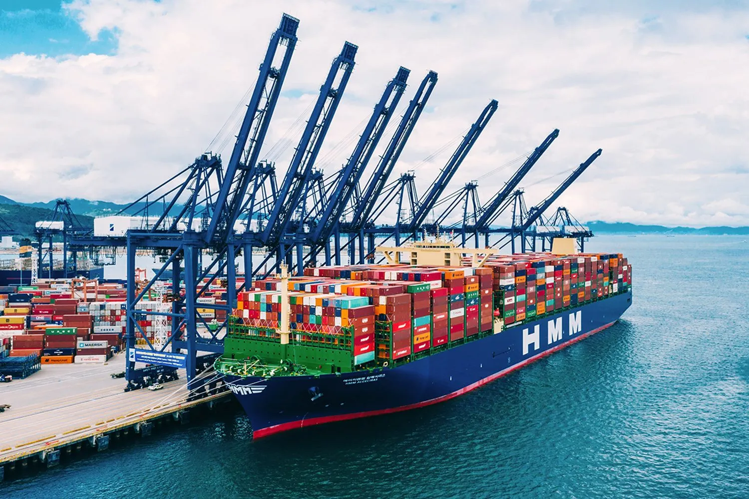 Container ship alongside blue cargo cranes at a busy port terminal